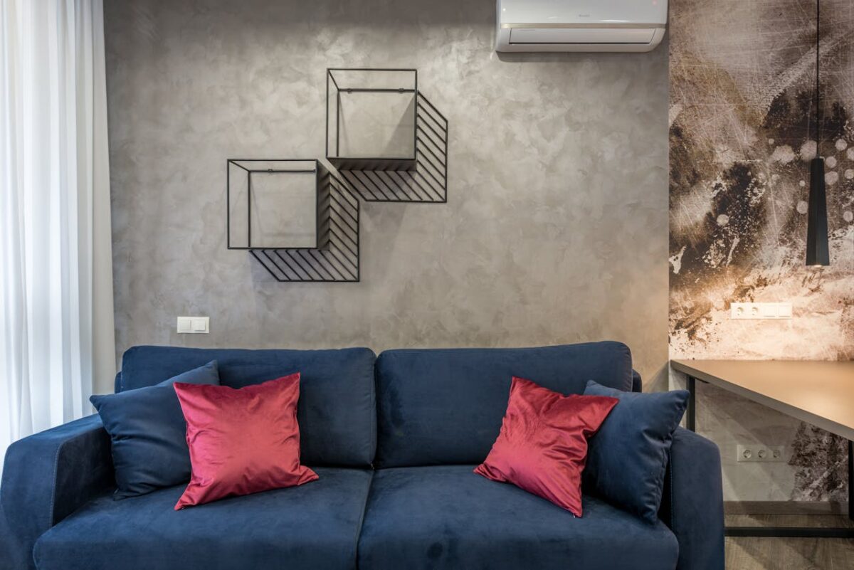Comfortable soft sofa with pillows placed in modern living room near wall with creative geometric shelves